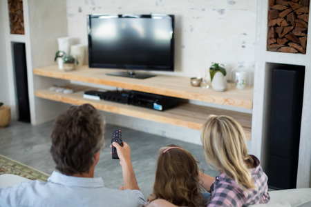 Rear view of family watching television in living room at homeの写真素材
