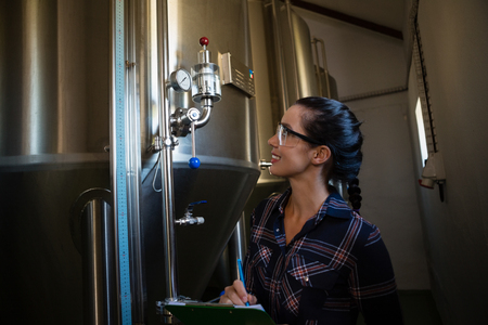 Smiling female worker examining storage tank at breweryの写真素材