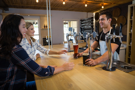 Bartender serving drinks to smiling female friends at counter in restaurant
