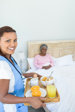 Portrait of smiling female doctor serving breakfast to senior woman in bedroomの写真素材