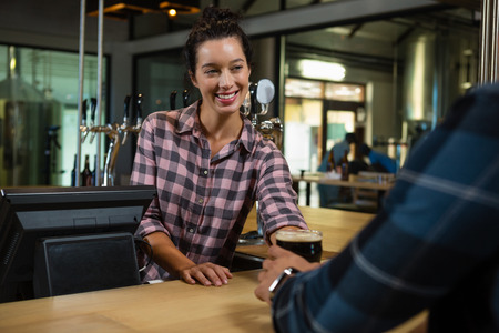 Smiling young barmaid serving drink to male customer at bar counter