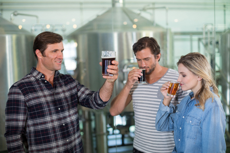 Friends tasting beer while standing by stoarge tank at factoryの写真素材