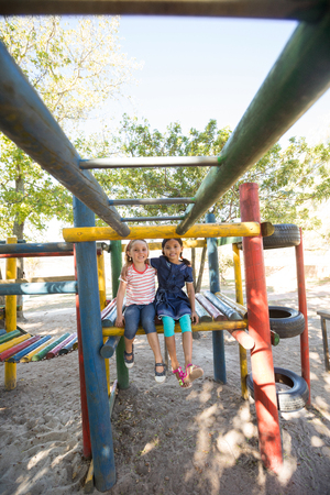 Portrait of smiling girls with arms around sitting on jungle gymの写真素材