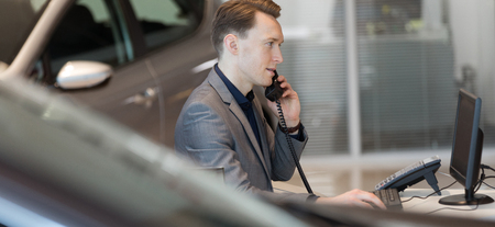 Sales talking on phone while using computer at desk in car showroom