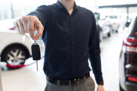 Midsection of salesman showing car keys while standing in showroomの写真素材