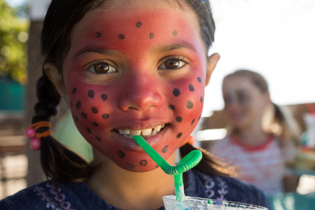 Close portrait up of girl with face paint having drink at parkの写真素材