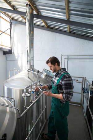 Male worker using digital tablet while examining vat at factoryの写真素材