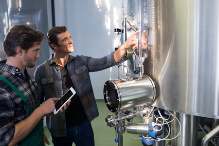Worker explaining to coworker using tablet computer at brewery