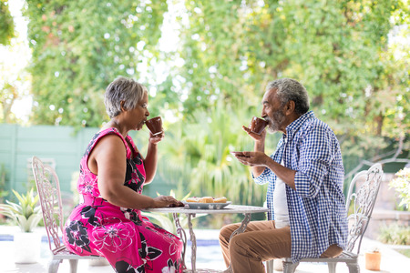 Side view of couple drinking coffee while sitting at table in yardの写真素材