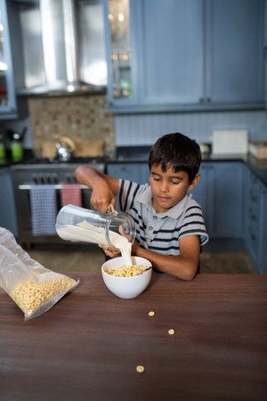 Boy pouring milk in cereals while having breakfast at home