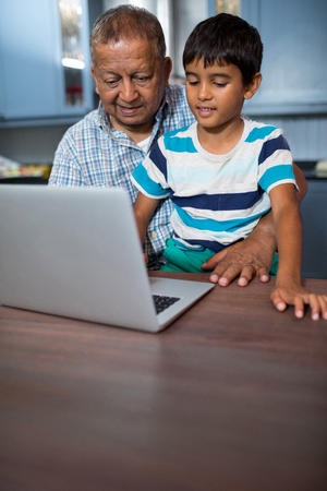 Grandfather with boy using laptop while sitting at tableの写真素材