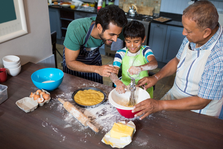 High angle view of father and grandfather looking at boy making food while standing in kitchen at homeの写真素材
