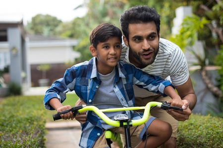 Father looking away while assisting son for cycling in yardの写真素材