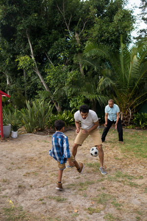Boy playing soccer with parents on field in yardの写真素材