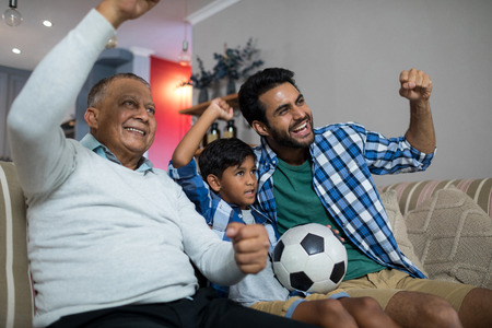 Happy family with arms raised watching soccer match while sitting on sofa at homeの写真素材