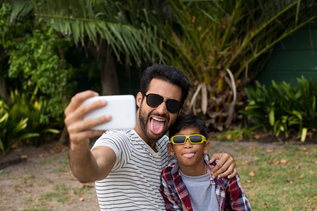 Playful father and son wearing sunglases while taking selfieの写真素材