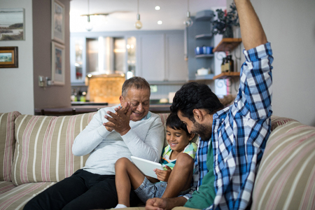 Happy grandfather and father with boy sitting on sofa in living room at homeの写真素材