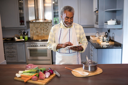 Smiling man using tablet computer while cooking food in kitchen at homeの写真素材