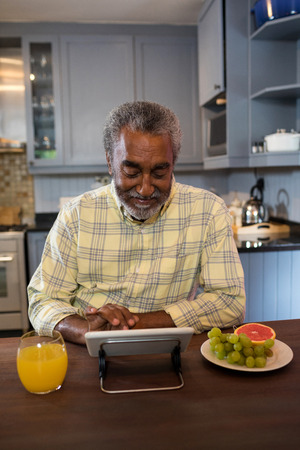 Smiling senior man using tablet computer at table in kitchenの写真素材