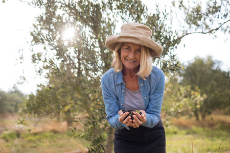 Portrait of happy woman holding harvested olives in farm on a sunny dayの写真素材