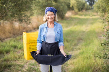 Portrait of happy woman holding harvested olives in her skirt on a sunny day