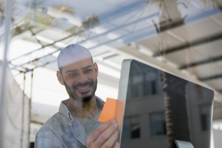 Smiling designer using computer in studio seen through glassの写真素材
