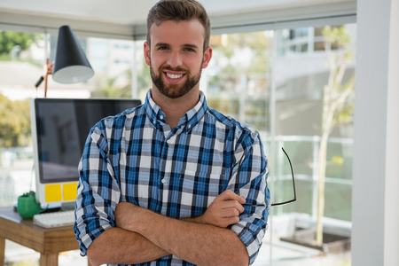 Portrait of smiling businessman with arms crossed standing in officeの写真素材