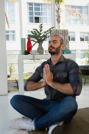 Businessman in prayer position meditating while sitting on floor at officeの写真素材