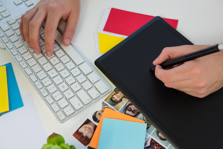 Cropped hand of designer writing on graphics tablet at desk