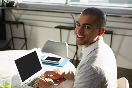 Portrait of businessman using laptop computer while sitting at desk in officeの写真素材