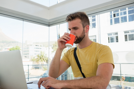 Businessman having drink while using laptop at desk in studioの写真素材