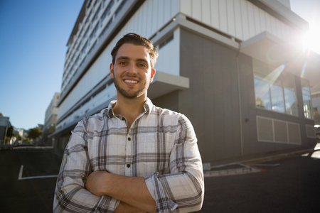 Portrait of smiling man with arms crossed standing by building in cityの写真素材