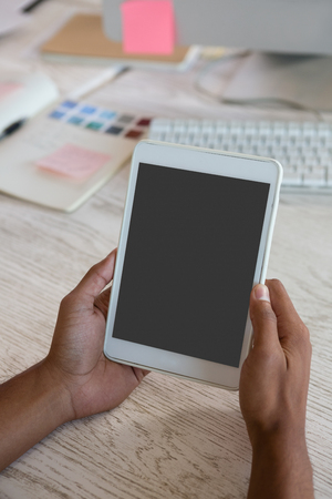 Cropped hands of man using tablet at desk in creative officeの写真素材