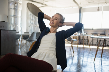 Thoughtful businesswoman with hands behind head relaxing on chair at officeの写真素材