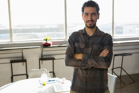 Portrait of confident young man standing against window at officeの写真素材