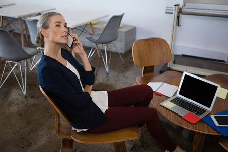 Businesswoman talking on phone while sitting on chair in office