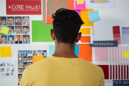 Rear view of young man standing against sticky notes in creative office