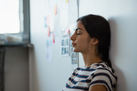 Tired young woman leaning on wall in creative officeの写真素材