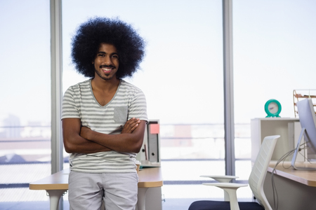 Portrait of smiling young man with arms crossed standing at officeの写真素材