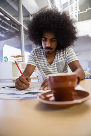 Young man writing on document at desk in officeの写真素材