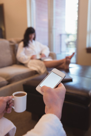 Man using mobile while having coffee in the living room at homeの写真素材