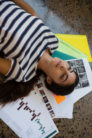 High angle view of thoughtful young woman lying on documents at creative office