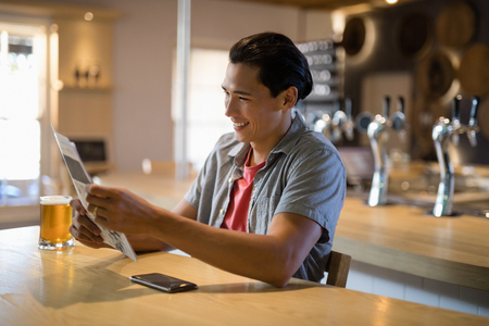 Smiling man reading newspaper in a restaurantの写真素材