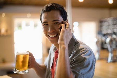 Portrait of man having beer while talking on mobile phone in a restaurantの写真素材
