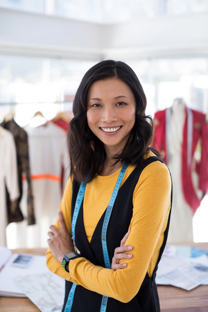 Portrait of smiling fashion designer standing with arms crossed in officeの写真素材
