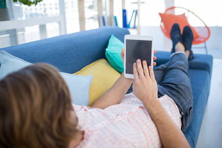 Male executive using digital tablet while relaxing on sofa in the officeの写真素材