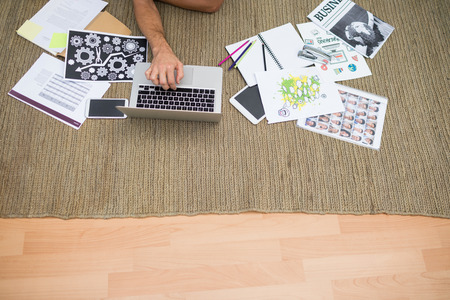 Male executive using laptop while lying on carpet in the officeの写真素材