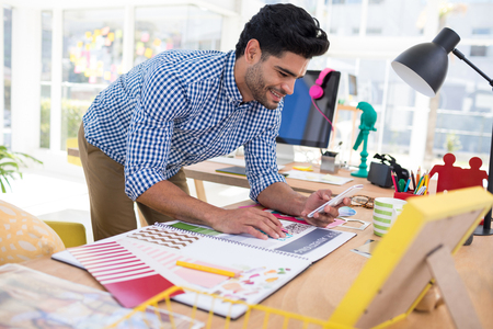 Male graphic designer using mobile phone while working at desk in the officeの写真素材