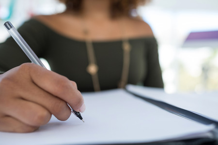 Mid-section of female executive writing on a document at desk in the office