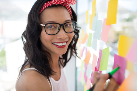 Portrait of female executive writing on sticky notes in officeの写真素材